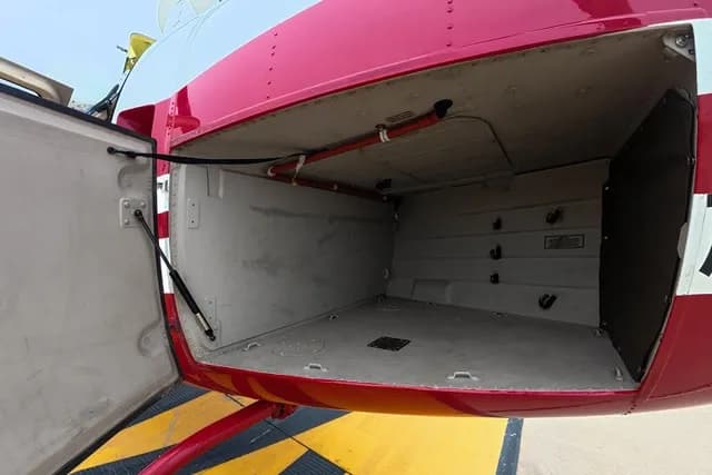 An open cargo compartment on the side of a red and white helicopter reveals its interior storage space.