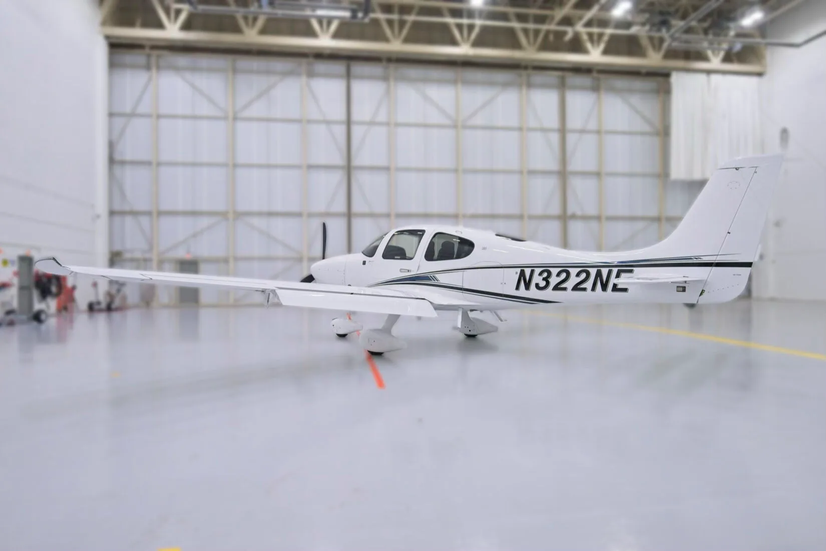 A side view of a white Cirrus SR22 aircraft with black and blue stripes, N322NE, parked in a hangar.