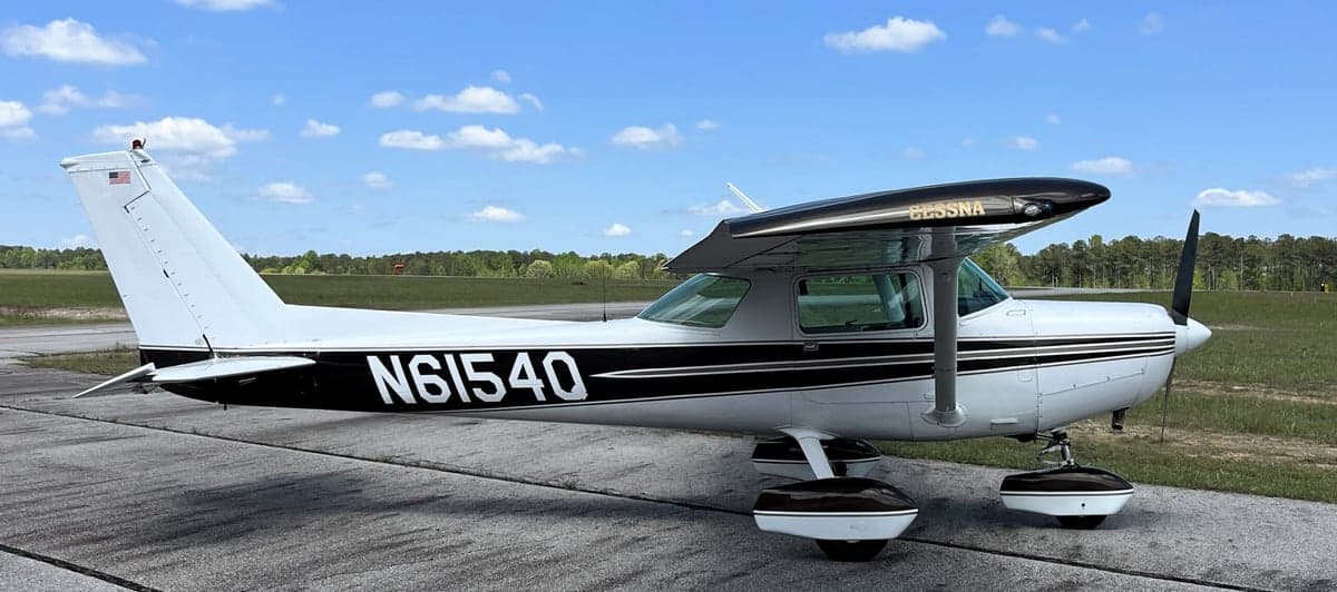 A Cessna 172 Skyhawk with a white and black paint scheme is parked on the tarmac.
