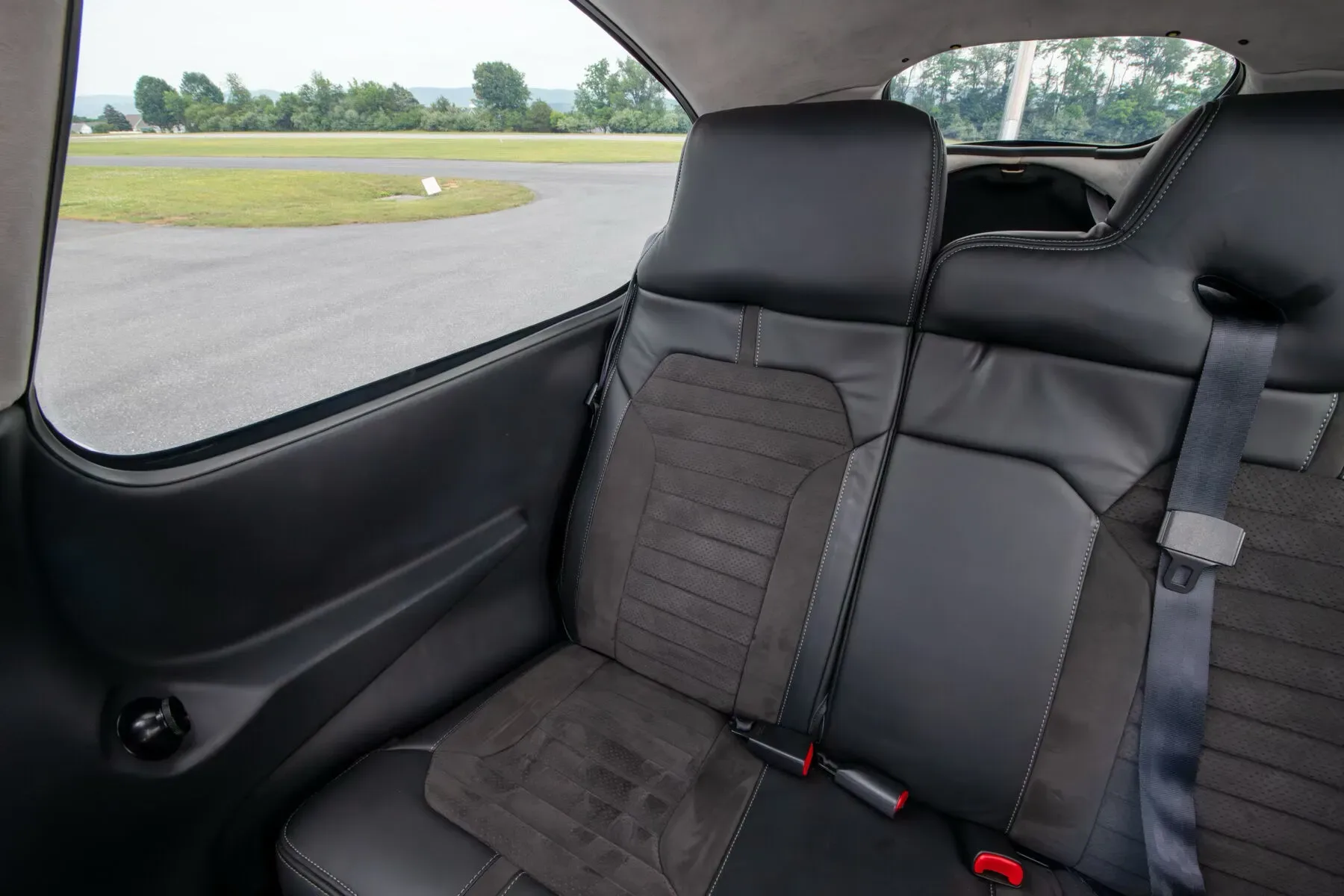 View of the black leather and suede rear seats in the aircraft cabin, looking out the window at the runway.