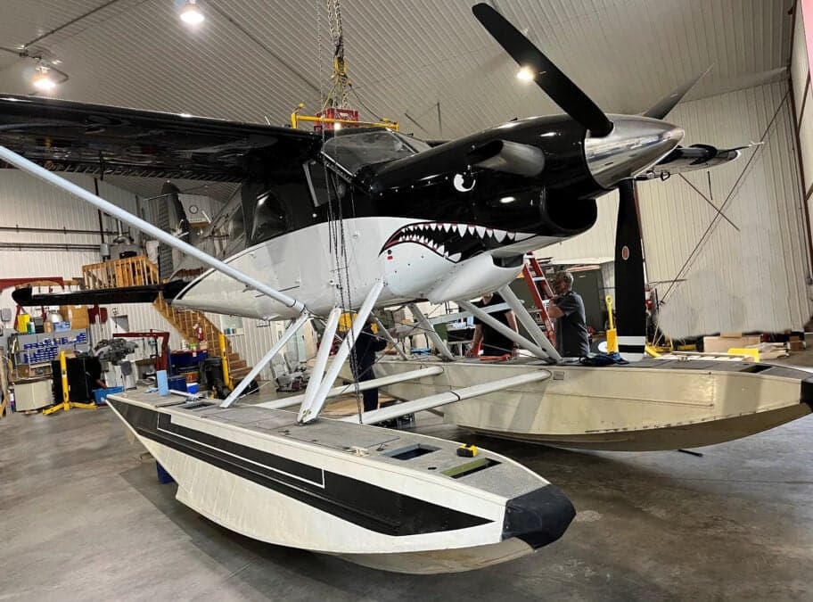 Seaplane with shark teeth paint scheme in a hangar, being worked on.