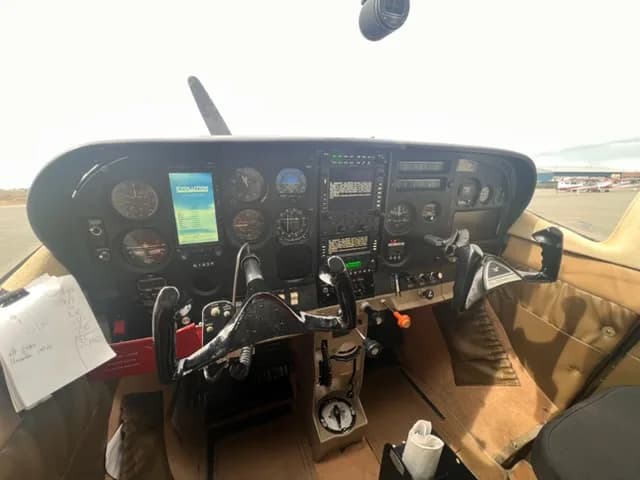 The cockpit of a Cessna 182 showing the instrument panel with analog gauges and a digital display.
