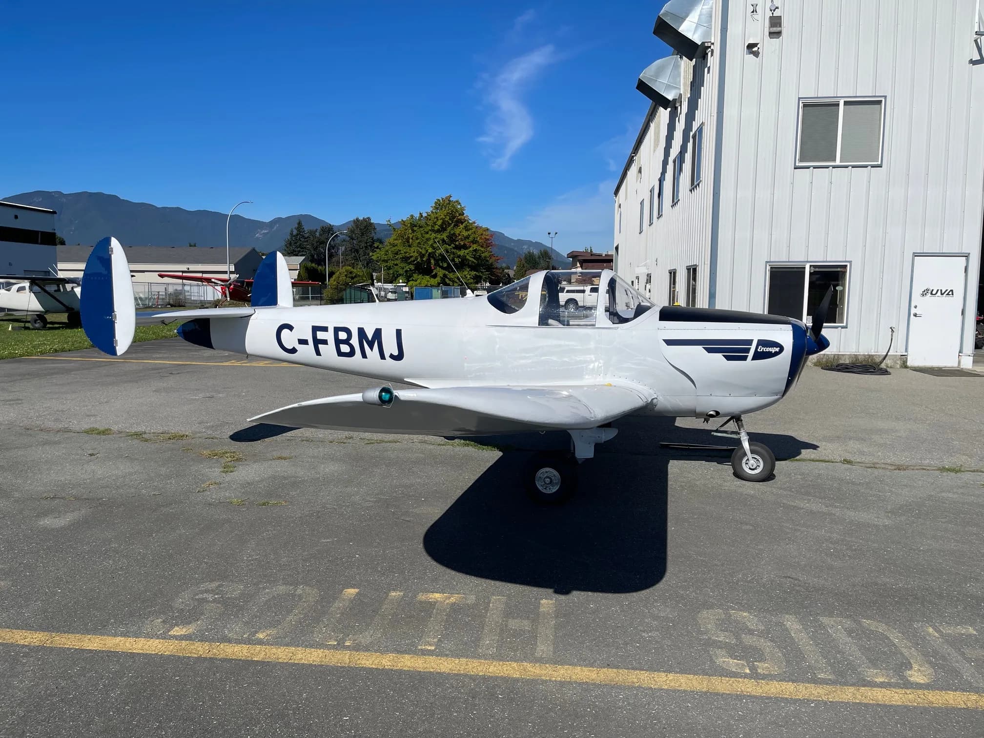 Side view of the Ercoupe CF-BMJ on the tarmac in front of a building.