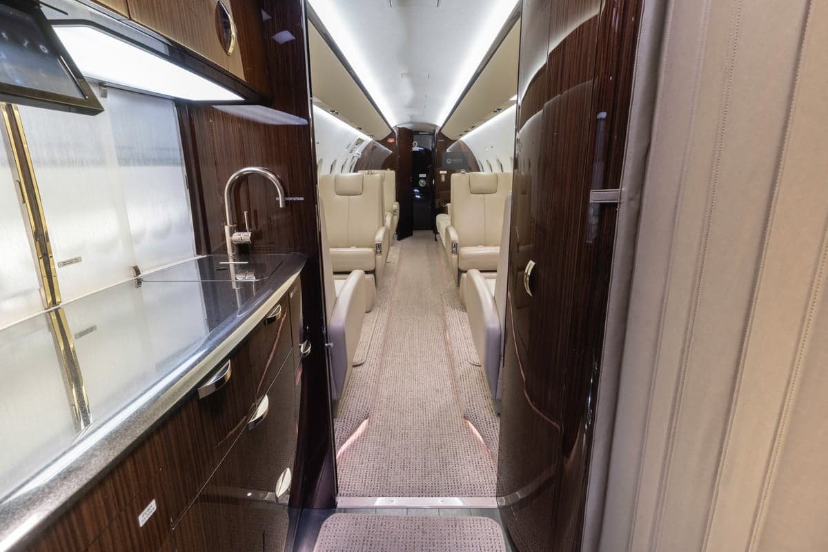 View down the aisle of a Gulfstream jet interior with wood paneling and cream-colored seats.