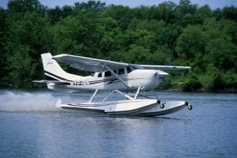 A white and red Cessna 206 on floats is docked on a lake.