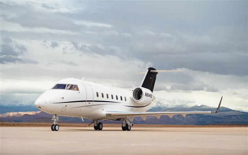 A white Bombardier Challenger 604, registration N604KE, parked on an airfield with mountains in the background.