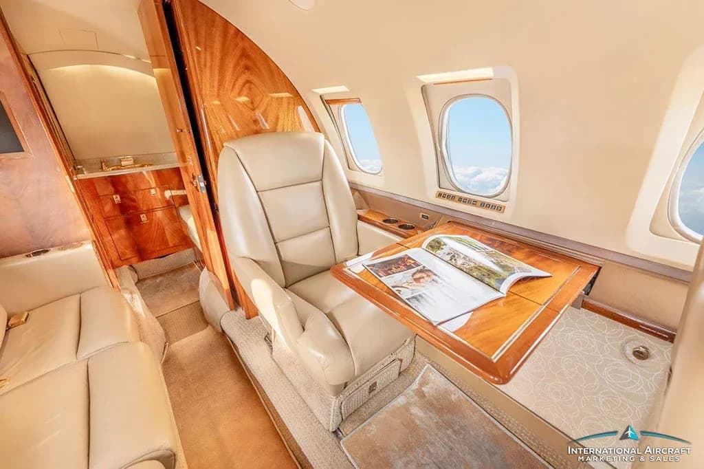 A single beige leather seat with a wooden fold-out table and magazine is shown in the private jet's cabin.