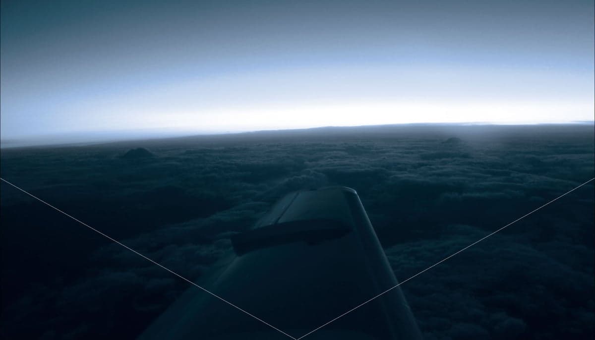 An aircraft wing is visible above a cloud layer at dusk.