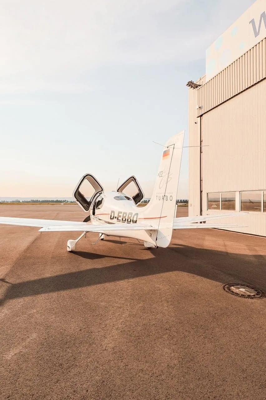A Cirrus aircraft with registration D-EBBQ parked near a hangar.