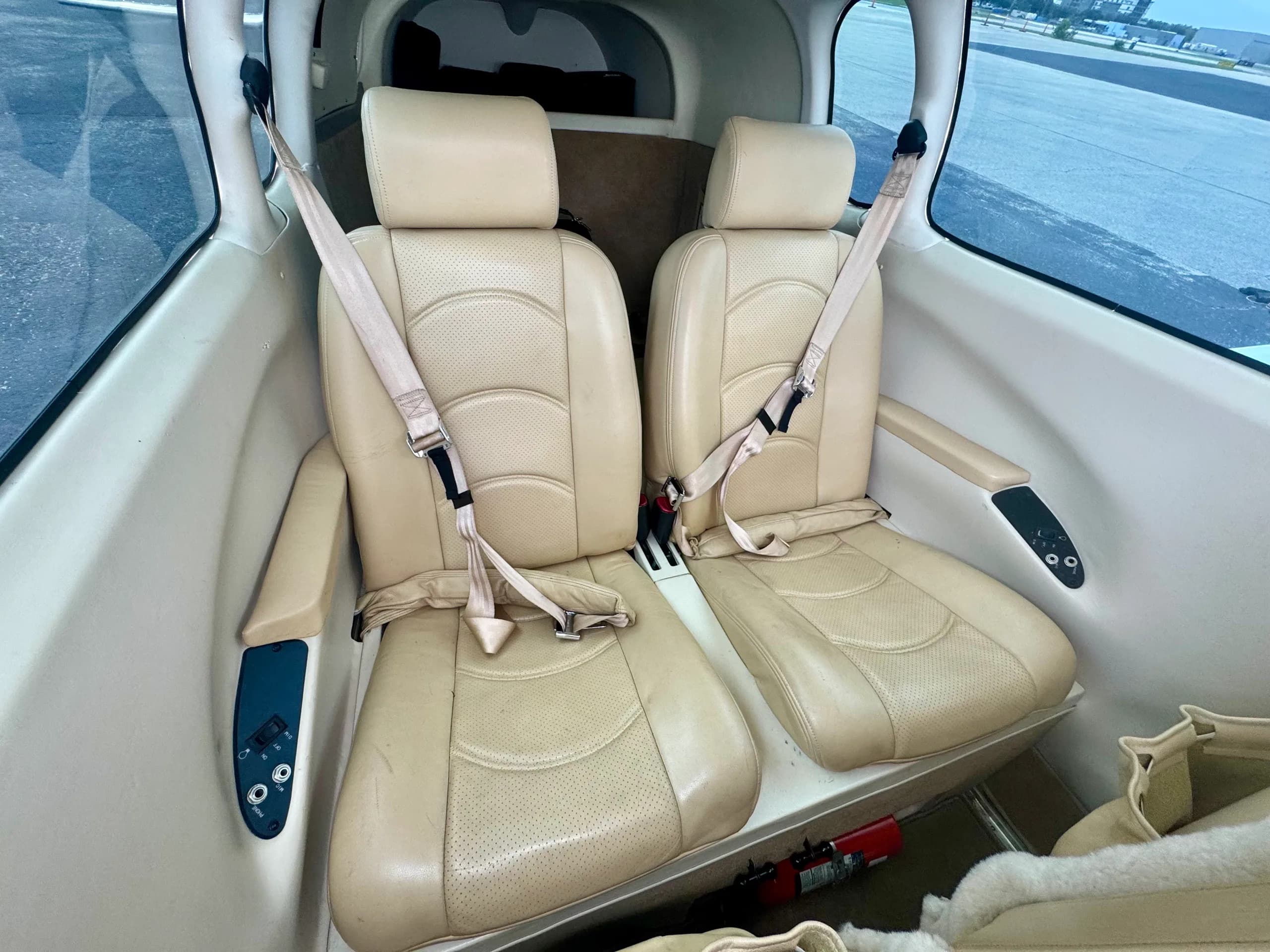 The rear cabin of a Mooney aircraft, showing two beige leather seats with seatbelts.