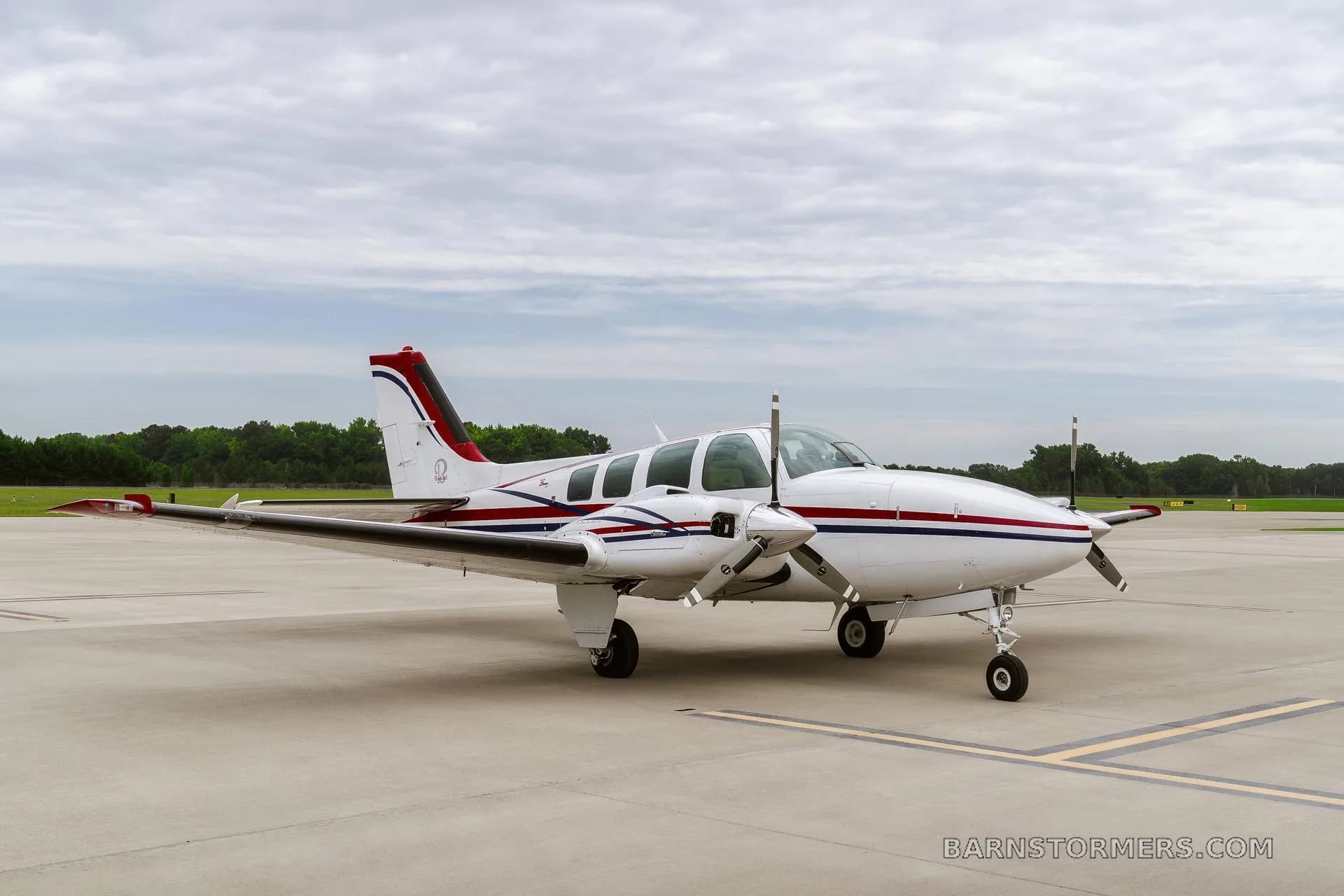 A front-quarter view of a white twin-engine propeller aircraft with red and blue stripes, registration N3194X, parked on an airfield.
