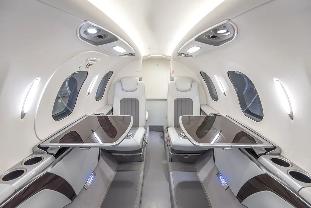 The interior cabin of a HondaJet HA-420, showing white and grey leather seats with fold-out tables deployed.