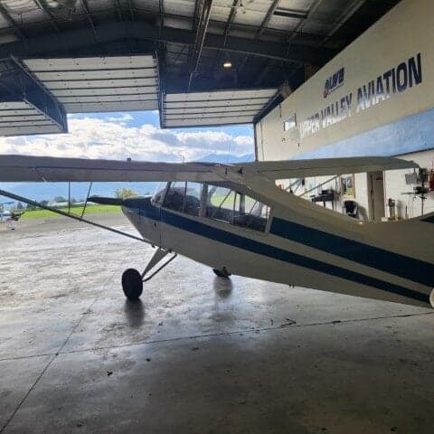 Side view of a white and blue aircraft parked inside a hangar with an open door.