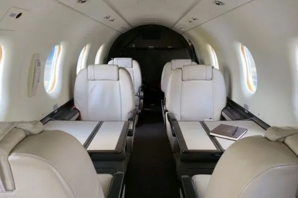 The aircraft's interior cabin featuring light-colored leather seats and fold-out tables, with a notebook on one table.