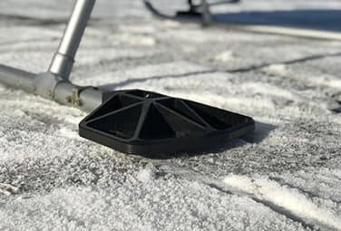Close-up of a helicopter skid landing pad on a snowy surface.