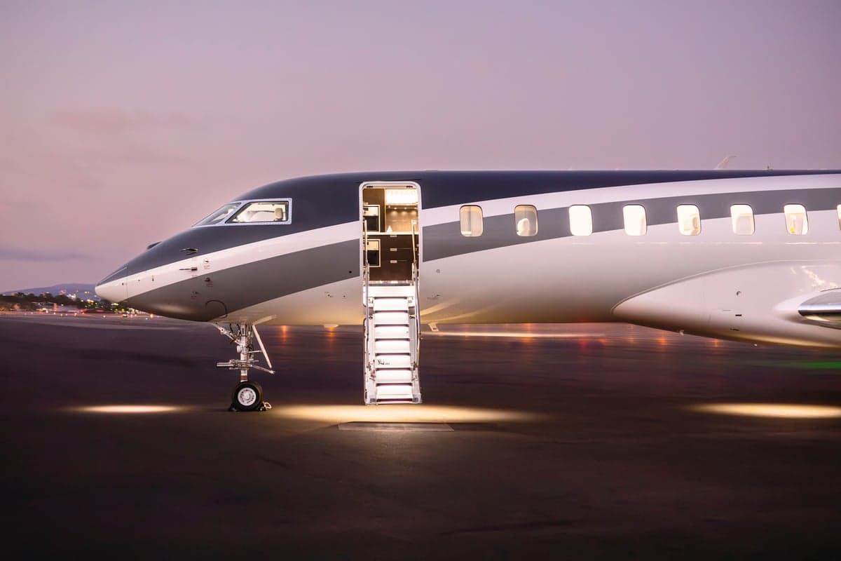 Exterior view of a private jet with the door open and stairs extended at dusk.
