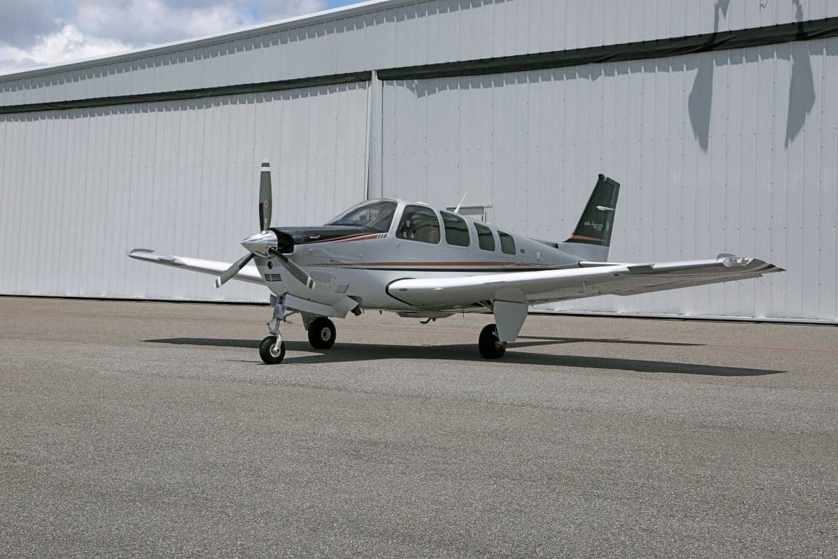 Side view of a Beechcraft Bonanza aircraft parked in front of a hangar.