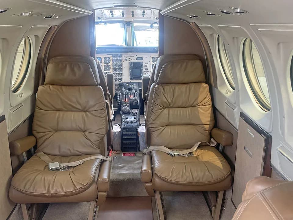 View from the aircraft cabin showing two tan leather seats facing forward, with the cockpit visible beyond.