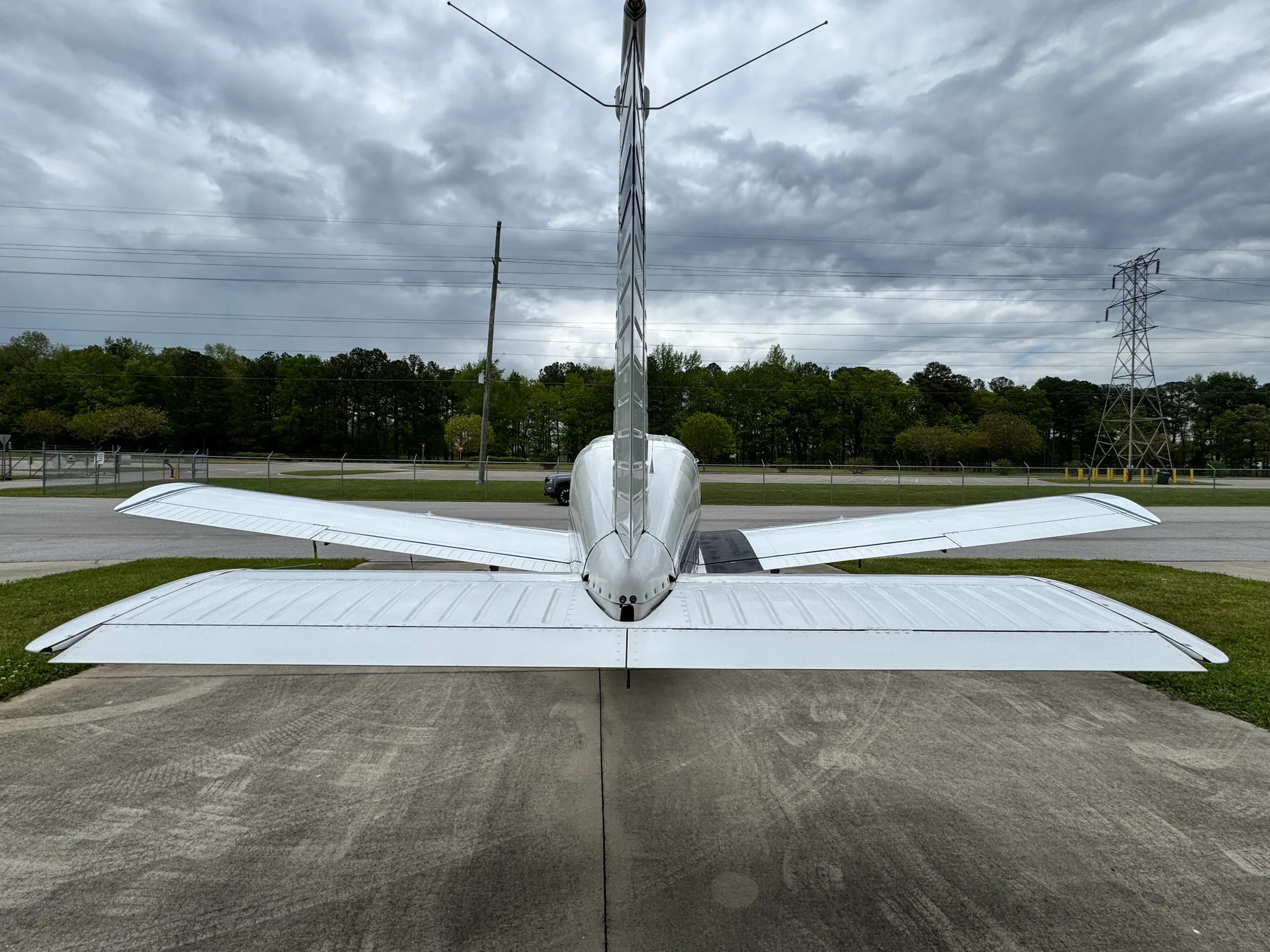 Rear view of a white single-engine aircraft, N15148, showing its tail and wings, parked on concrete under a cloudy sky.