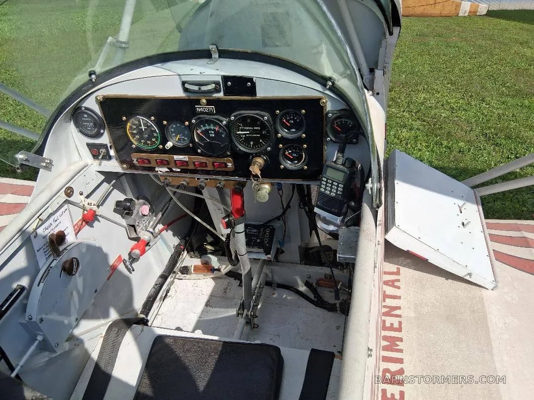 The cockpit of a biplane, showing the instrument panel with gauges, controls, and a handheld radio.