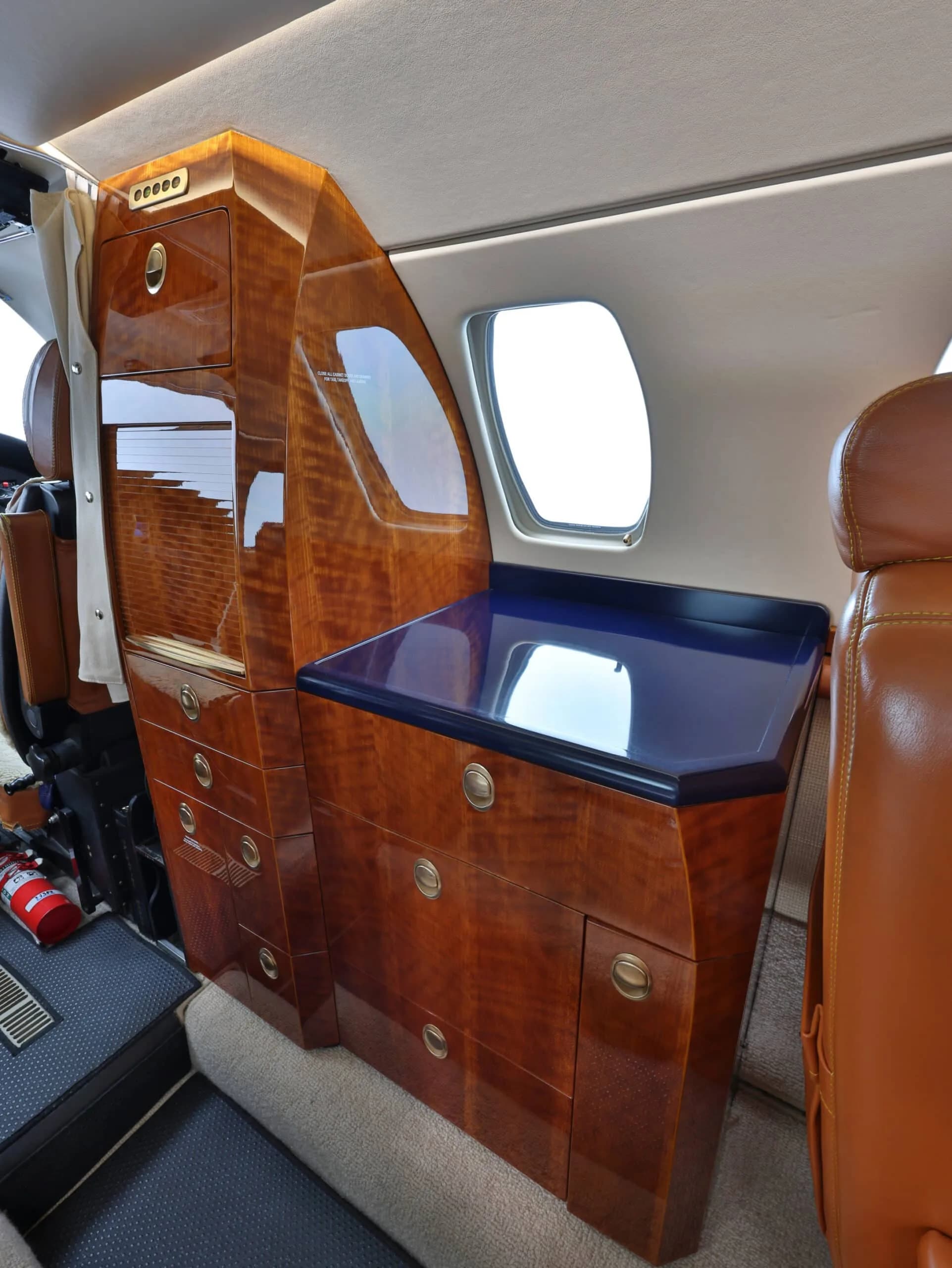 Interior view of a private jet showing a polished wooden galley cabinet with a blue countertop.