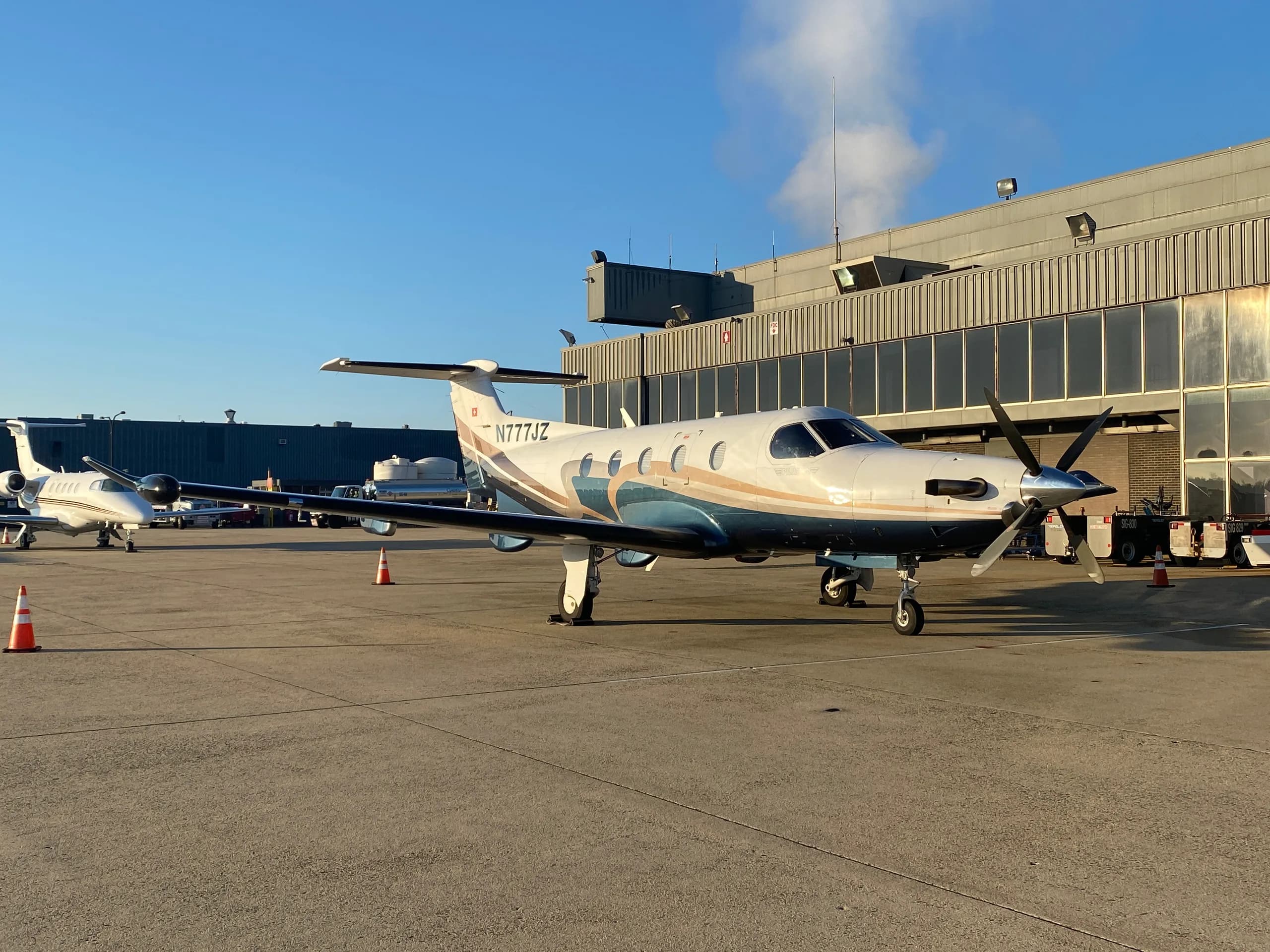 A Pilatus PC-12 aircraft with registration N777JZ is parked on the tarmac next to a building.