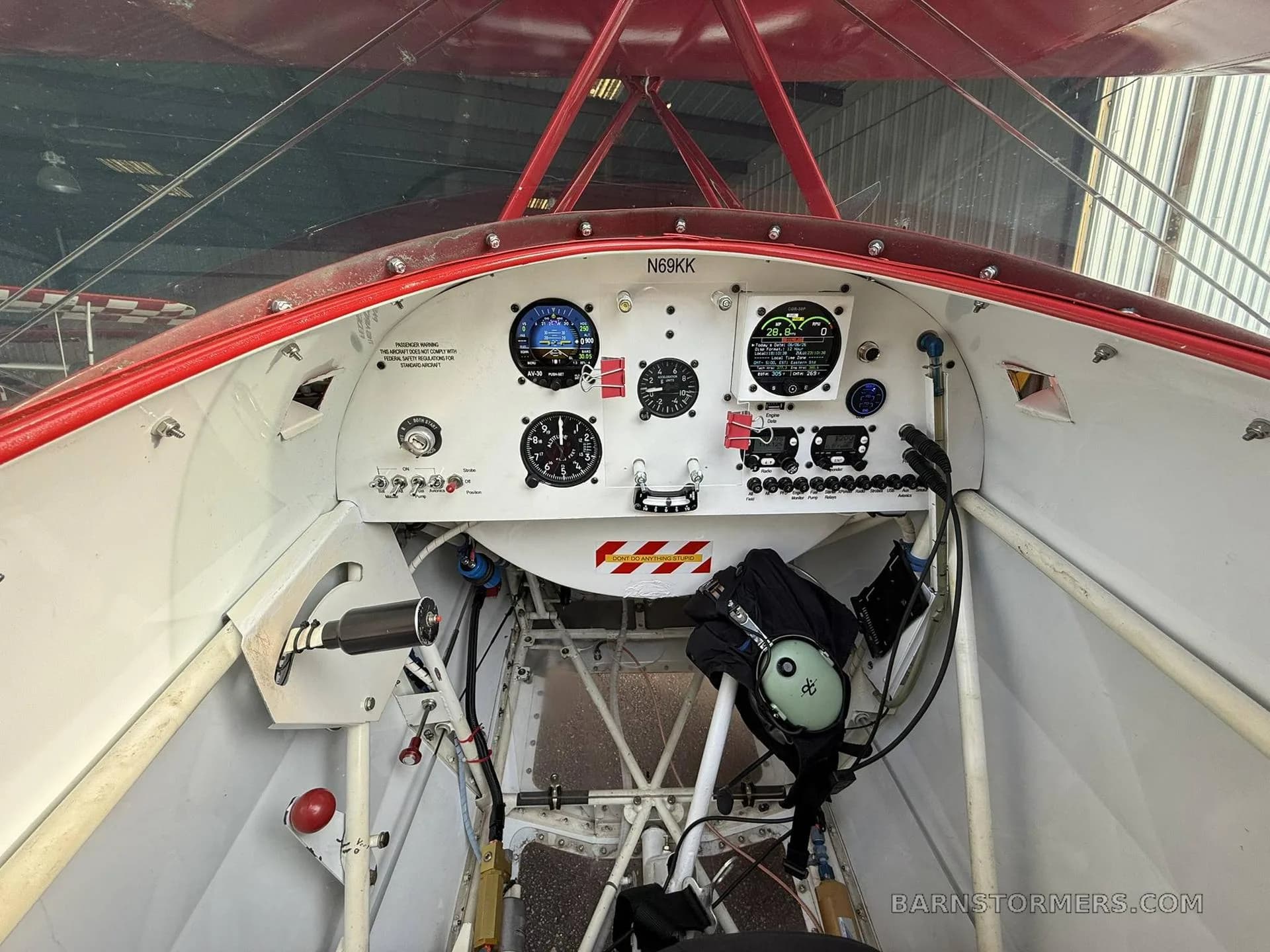 The cockpit of a red and white biplane shows the instrument panel with various gauges and controls.
