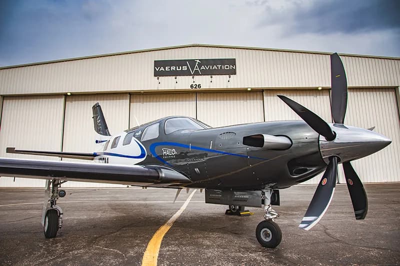 A gray and white HALO equipped aircraft is parked in front of a hangar.