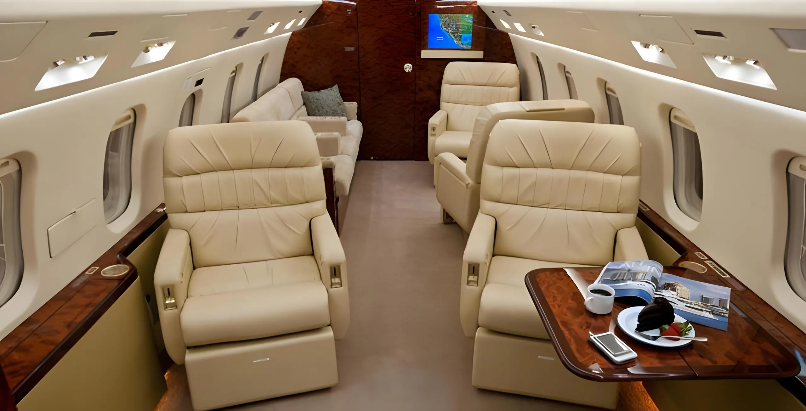 The aircraft's elegant cabin interior with beige leather seating, a wooden table set with a snack and magazine, and a map displayed on a screen at the back.