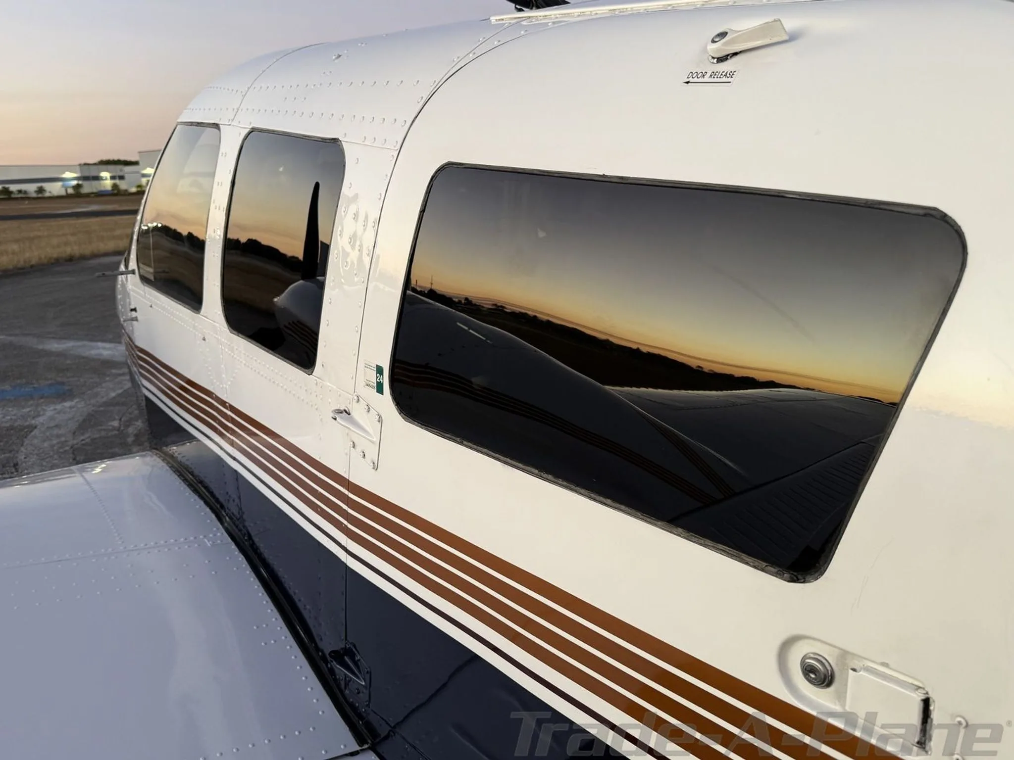 A close-up of the Piper Seneca III's cabin windows, reflecting the sunset colors.