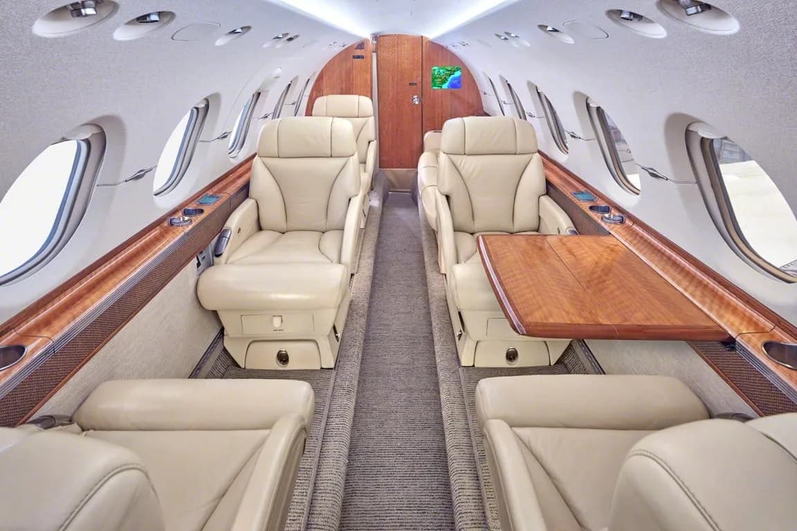 The luxurious interior cabin of a private jet with beige leather seats and polished wood accents.