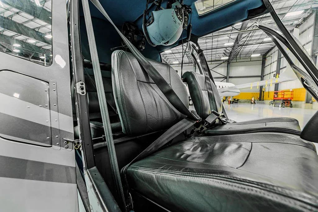 The black leather seats and interior of a helicopter cabin, with a headset hanging above.