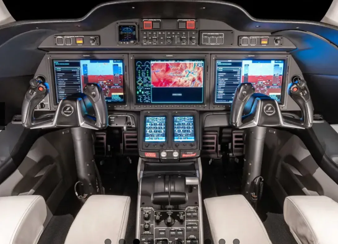 The modern cockpit of a HondaJet, featuring multiple large display screens and dual control yokes.