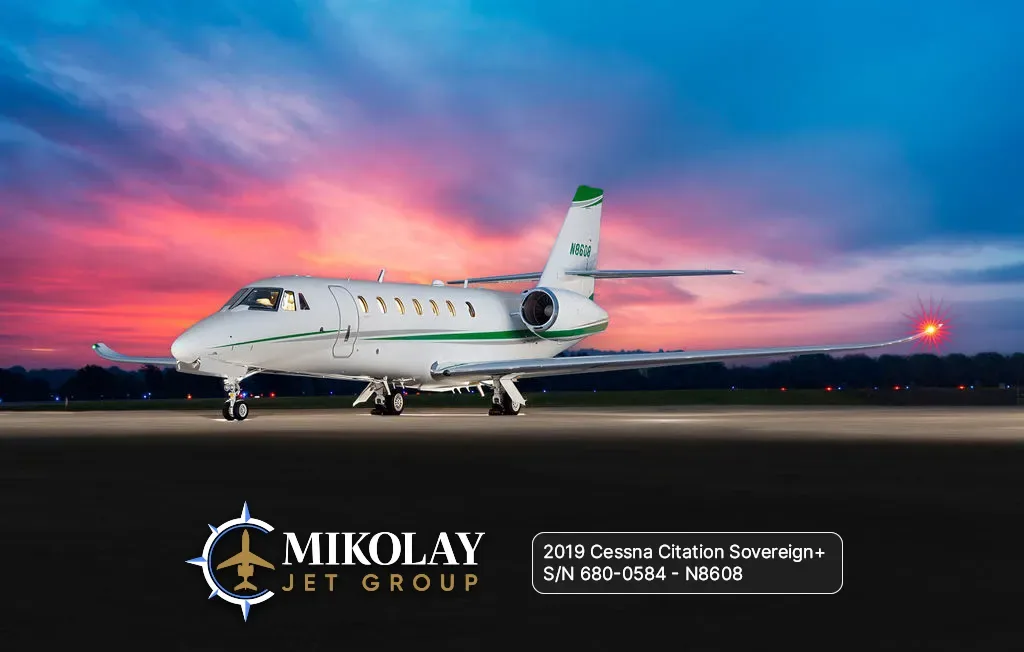 A white Cessna Citation Sovereign+ business jet with green accents on the tail and fuselage, parked on a tarmac at sunset.