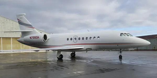 A white Dassault Falcon 2000 business jet, registration N700CH, with red and grey stripes, parked on a wet tarmac.