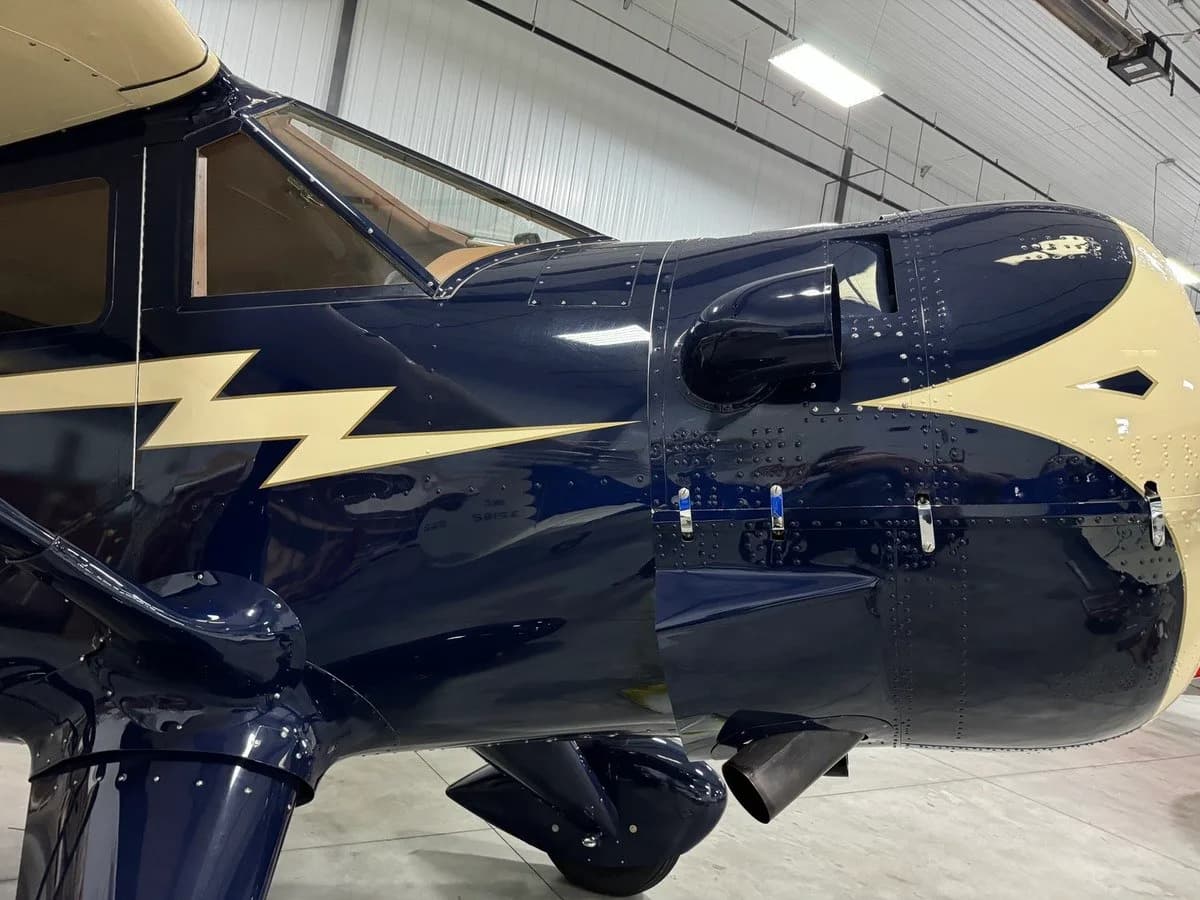 A close-up of the front fuselage and engine cowling of a dark blue and cream vintage aircraft, showing the lightning bolt detail.