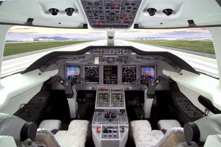 The modern cockpit of a private jet with multiple digital displays and controls, looking out onto a runway.