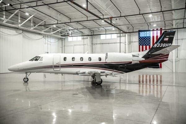 A Citation jet, N338HR, is parked in a hangar with an American flag in the background.