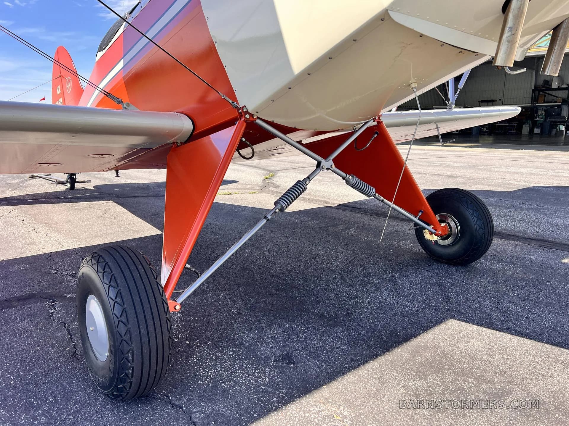 A close-up view of the red biplane's landing gear with large tires and spring suspension.