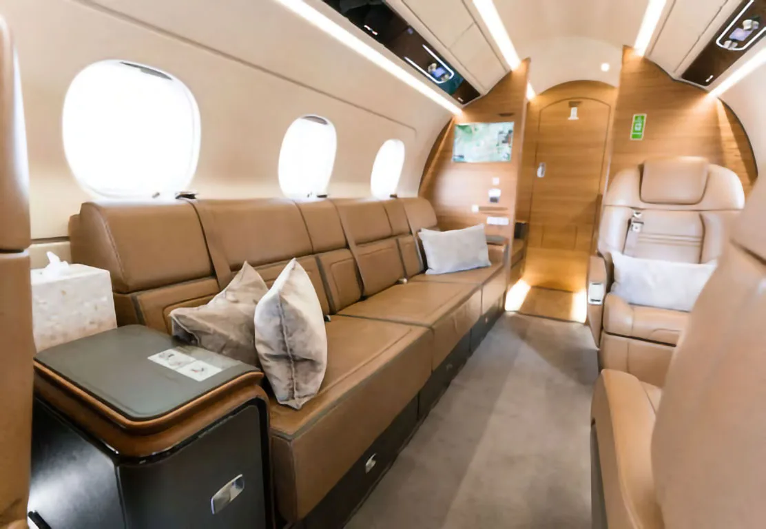 A view of the business jet's cabin showing a long tan leather sofa and individual seats.