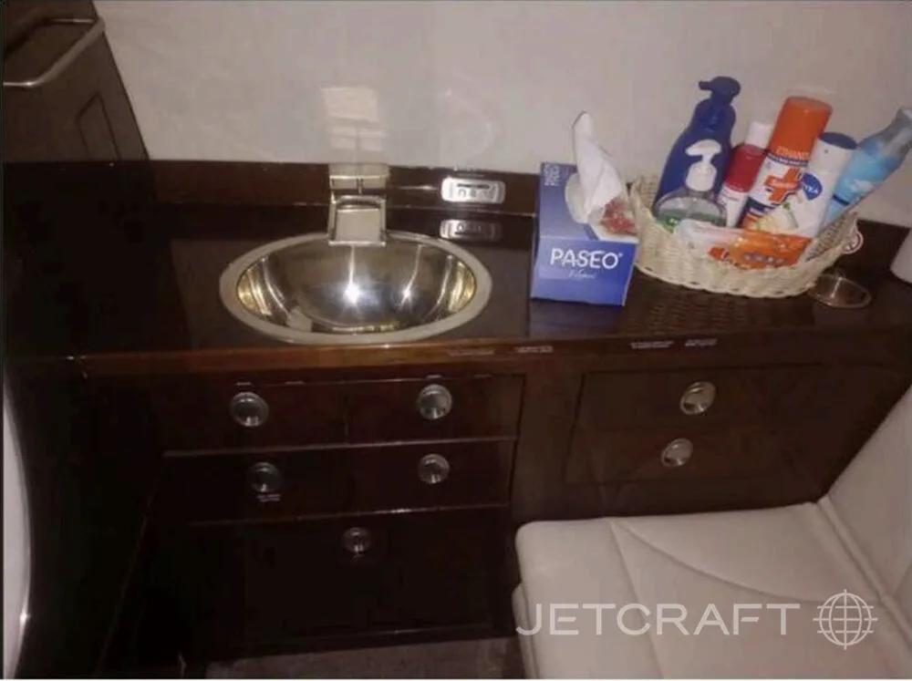 A close-up of a stainless steel sink set into dark wood cabinetry, with toiletries in a basket.