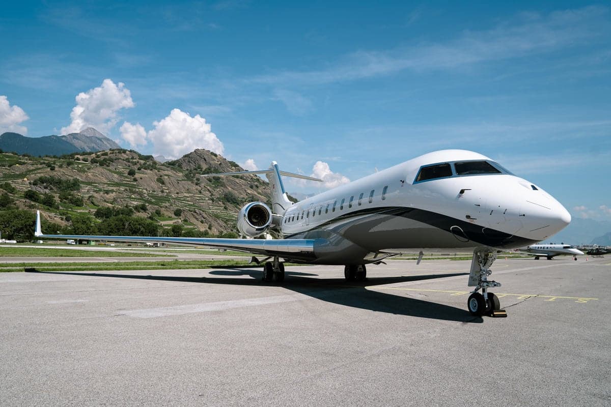 A Bombardier Global XRS aircraft parked on the tarmac with mountains in the background.