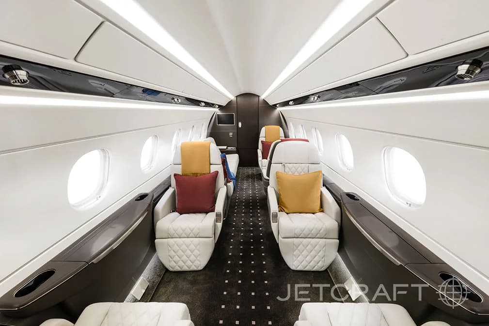 The interior of a jet aircraft with white leather seats and colorful pillows.