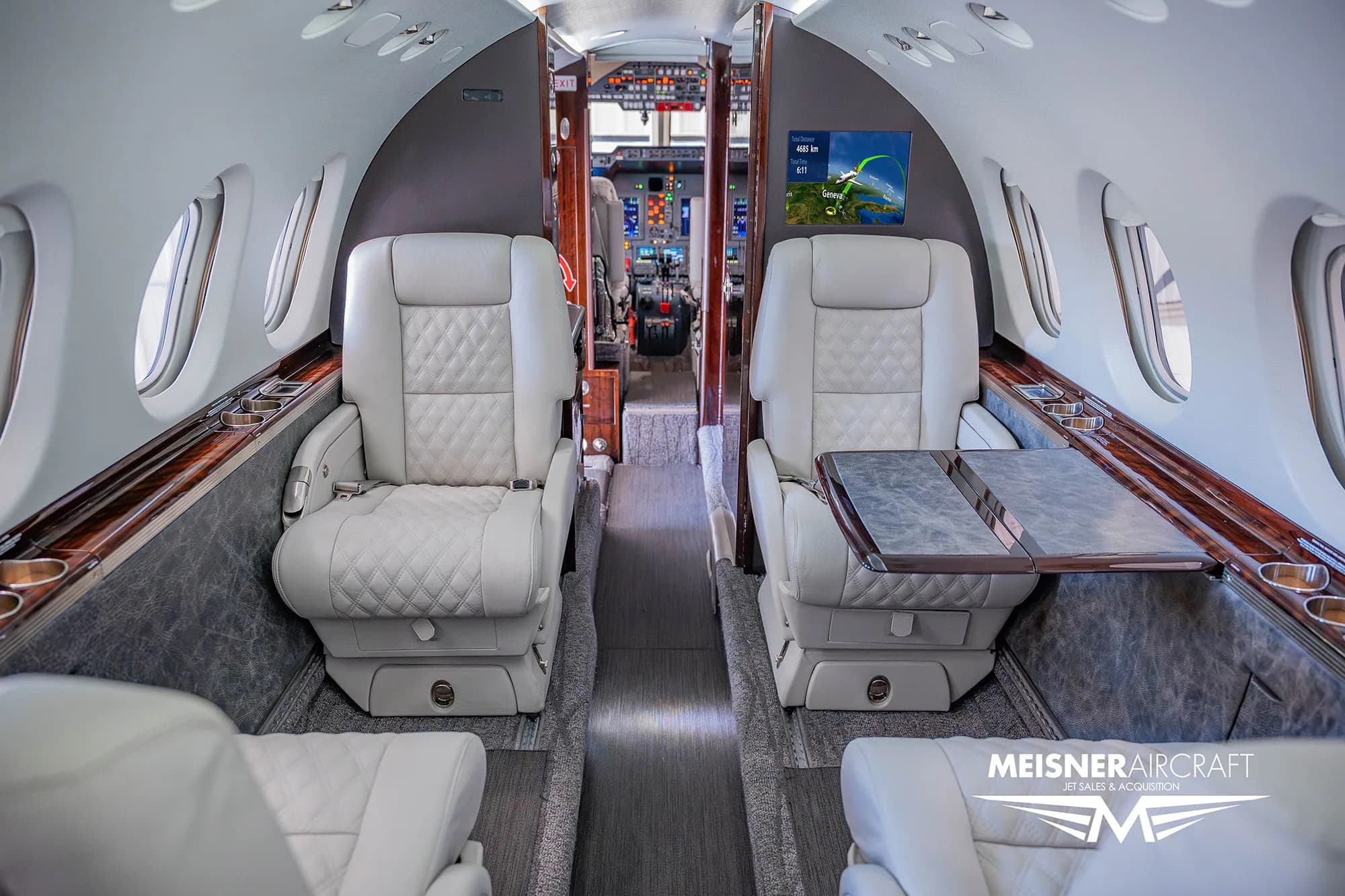 The luxurious white leather interior cabin of a business jet, looking towards the cockpit.