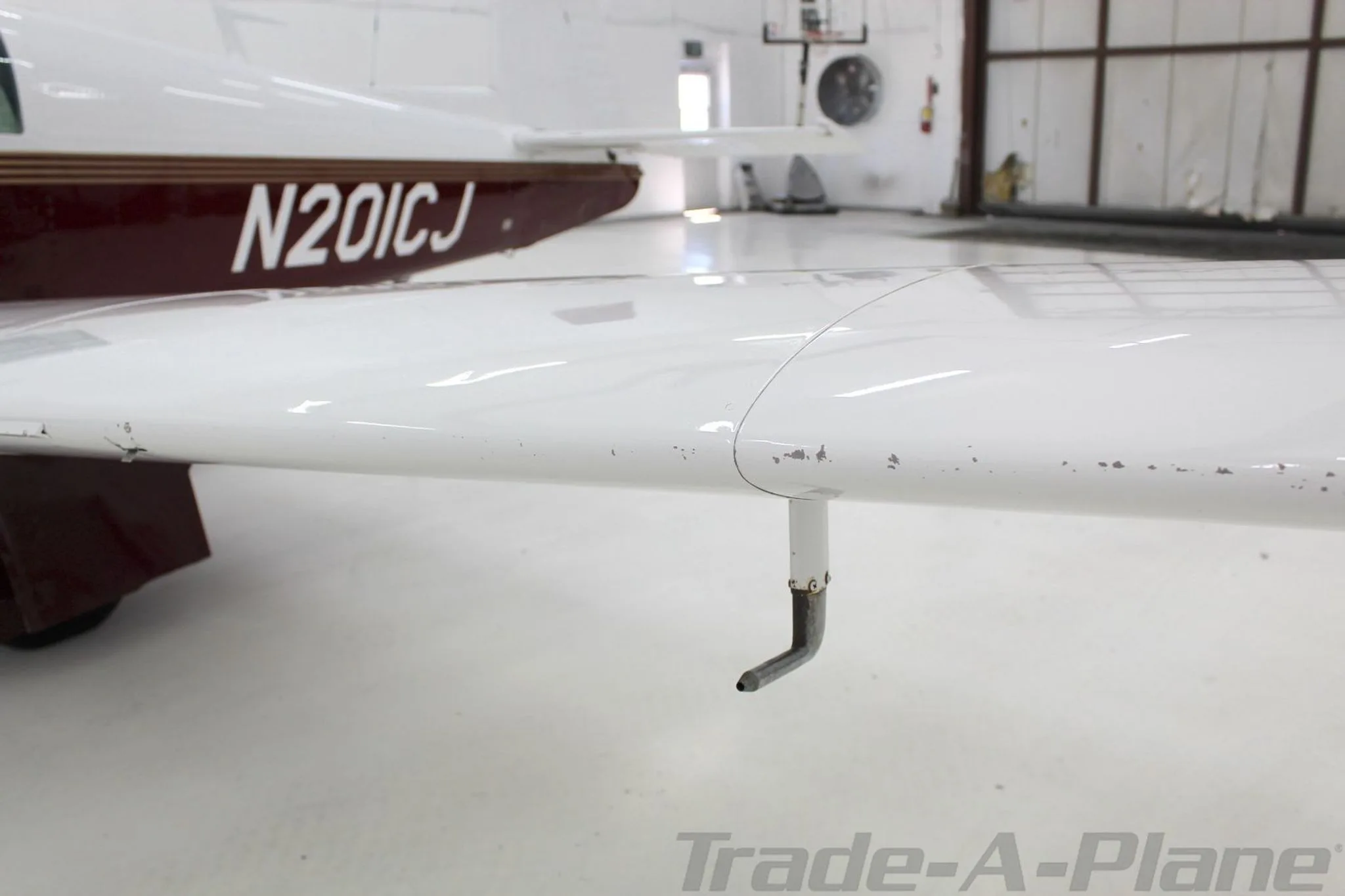 A close-up view of the leading edge of the Mooney M20J's wing, showing a pitot tube and minor paint wear.