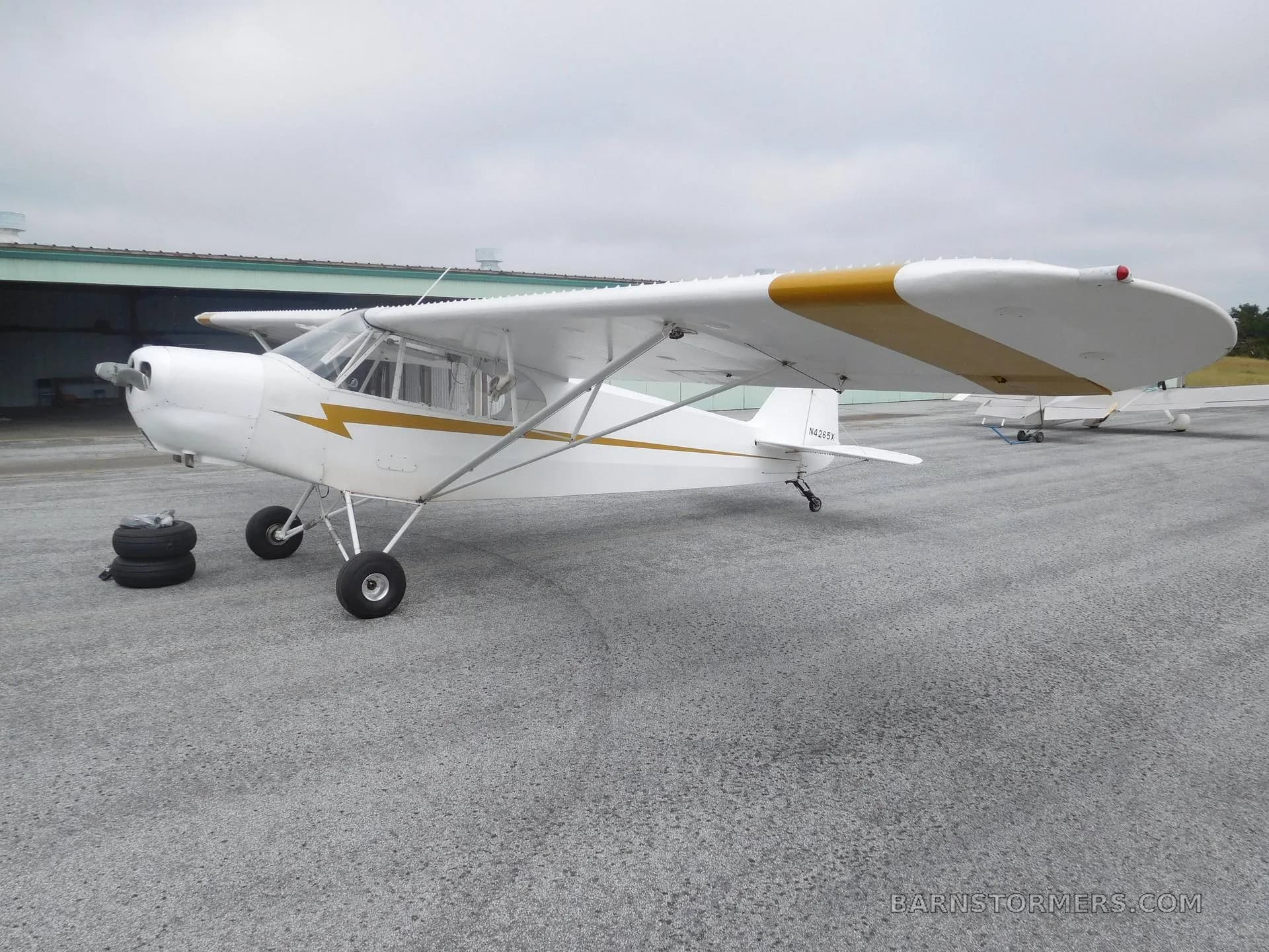 A white experimental aircraft with gold wing stripes is parked on an asphalt surface next to a hangar.