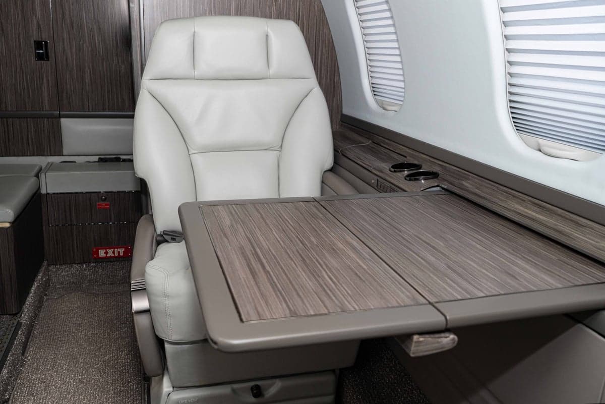 A single white leather seat with a wooden table in the aircraft cabin.