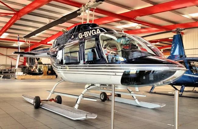 A blue and white Bell helicopter with registration G-BVGA is parked inside a hangar.