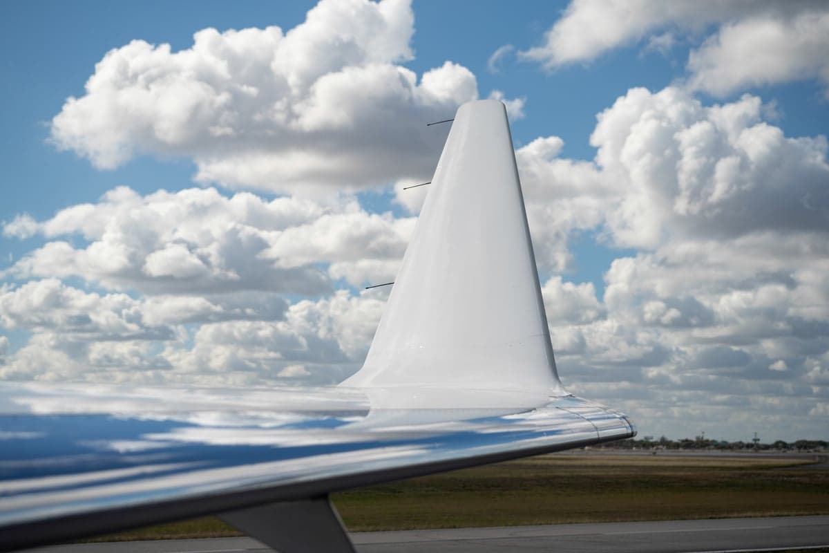A close-up of the white winglet and reflective wing surface of a business jet on an airfield under a cloudy sky.