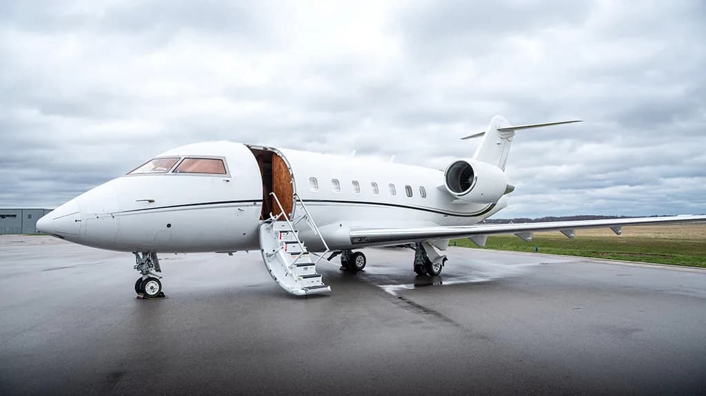 A white business jet with its main cabin door open and airstairs deployed on a tarmac.